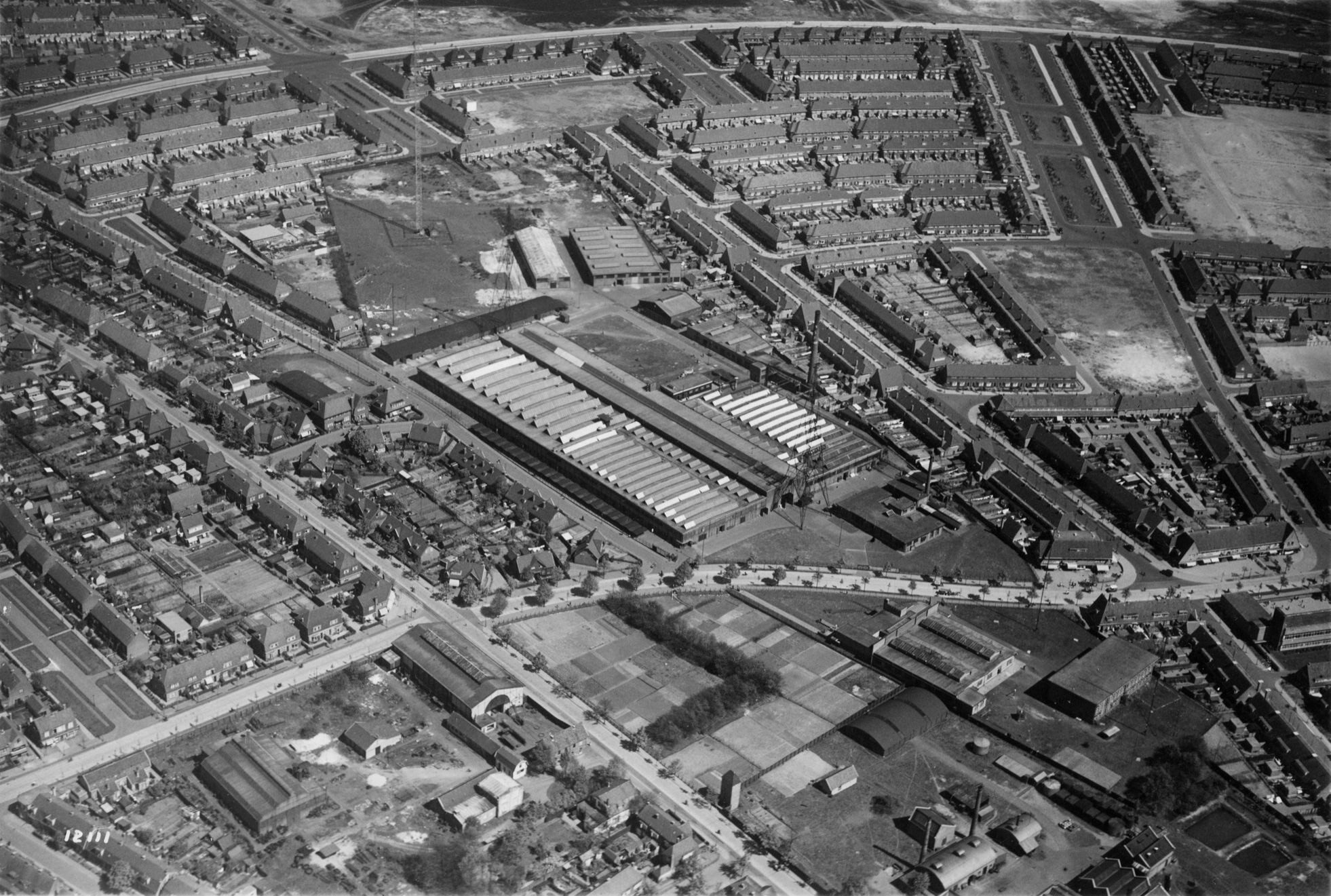 Luchtfoto van de NSF-fabriek en de buurt over 't spoor vlak voor de oorlog, met de twee Zingende Torens zichtbaar naast de fabriekshal